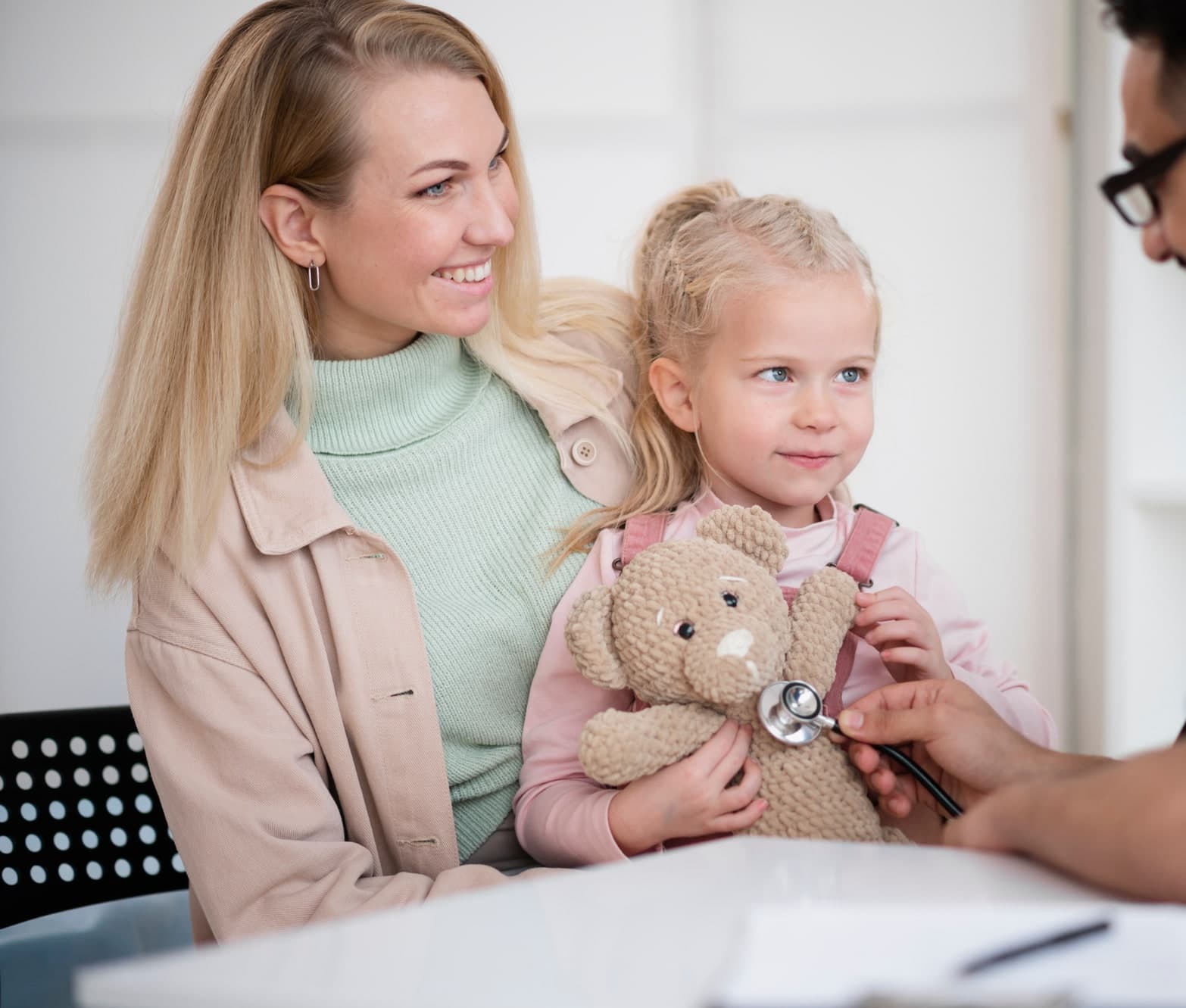 A mother and her daughter with a provider listening to a teddy bear's heartbeat